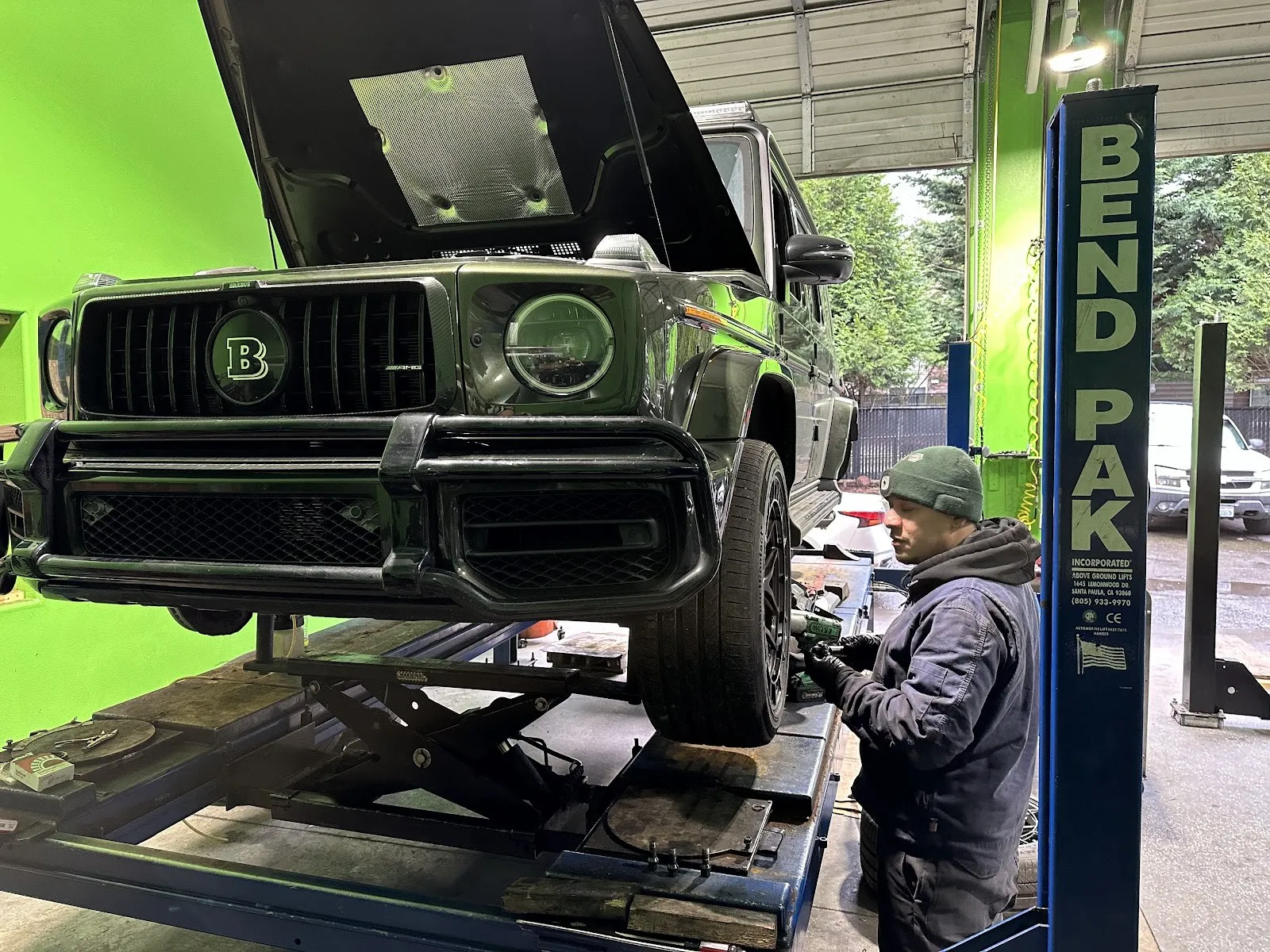 A technician working under a black G-Wagon on the lift, in the bright green bay